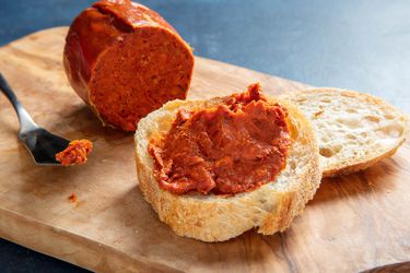 'Nduja next to a slice of bread slathered with 'nduja and a knife on a wooden block.
