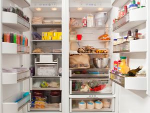 An open refrigerator stocked with various groceries and food items on the shelves and compartments including beverages and produce