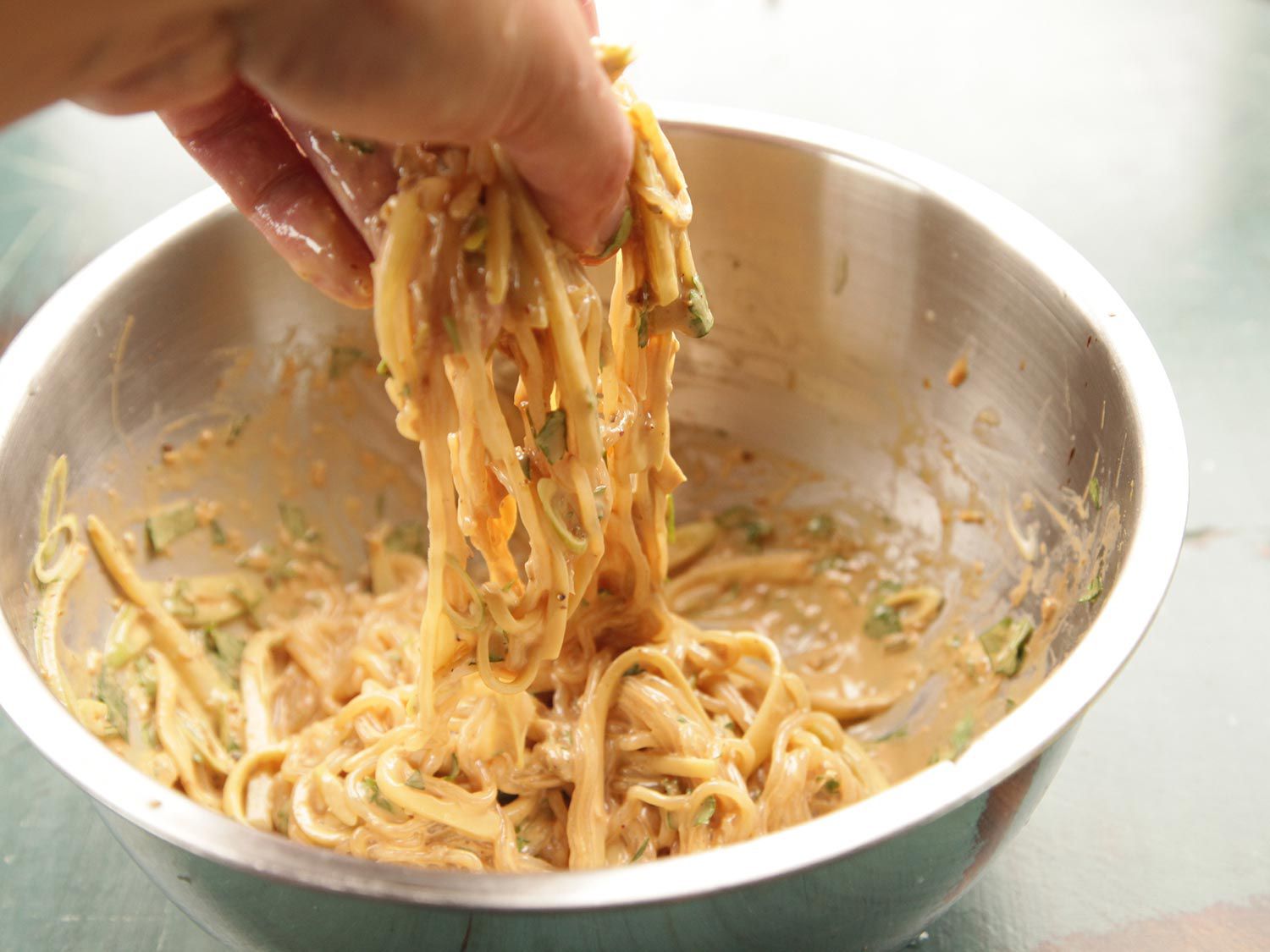 Tossing shiritaki noodles with sauce using a hand.