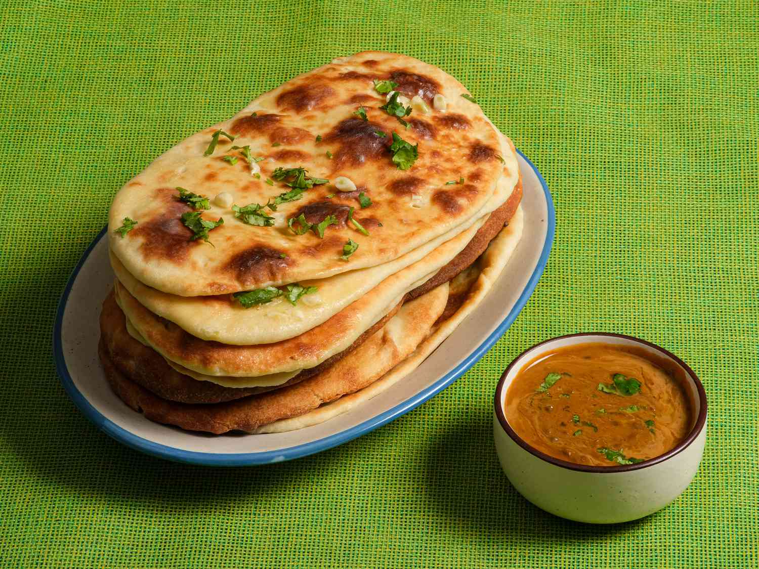 Stack of garlic naan on a white plate on a lime green tablecloth with a side of chutney 