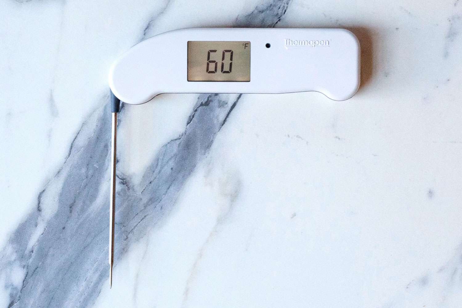 A white Thermapen ONE thermometer with its probe extended on a marble countertop.