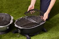 A person placing grilling grates onto the PK grills grill.