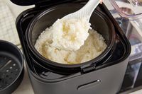 Cooked rice being scooped out of the KitchenAid rice cooker.