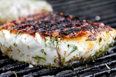 A fish fillet seasoned with herbs being cooked on the grill. 