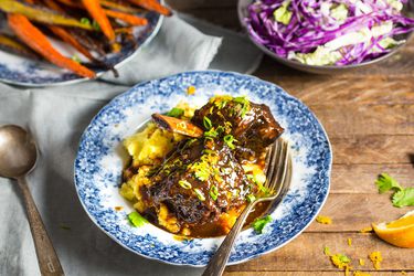 Blue and white bowl of a braised shortrib dinner with bowls of roasted carrots and cabbage in background