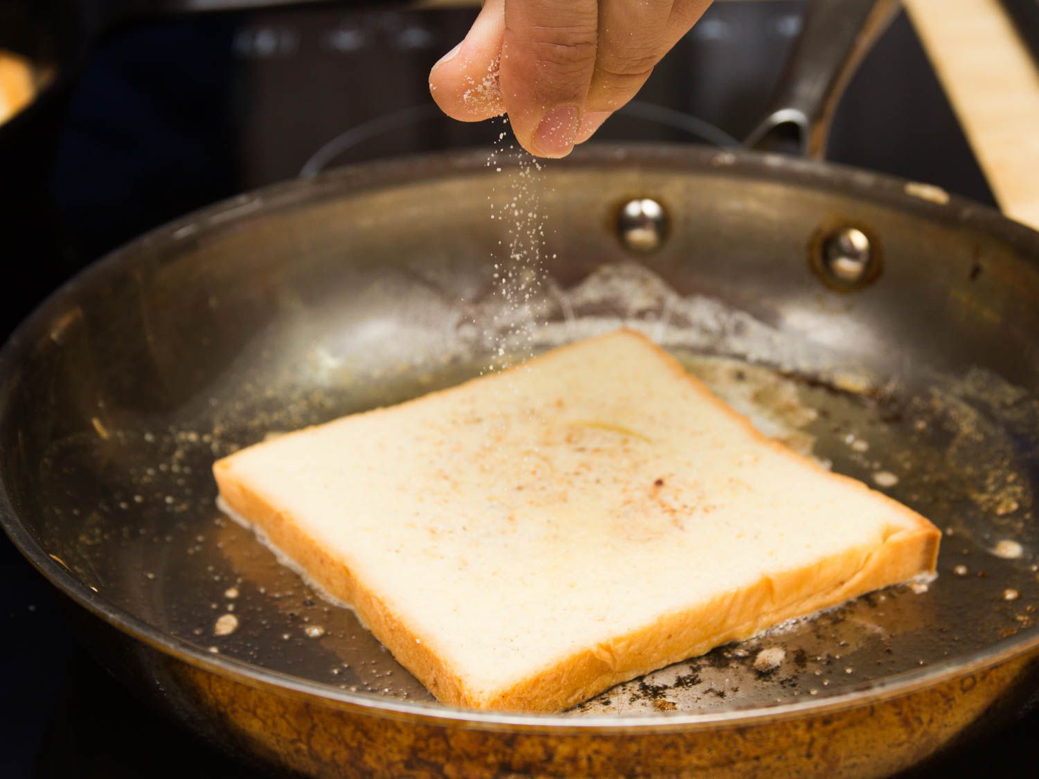 Sprinkling sugar on a slice of French toast cooking in a skillet.