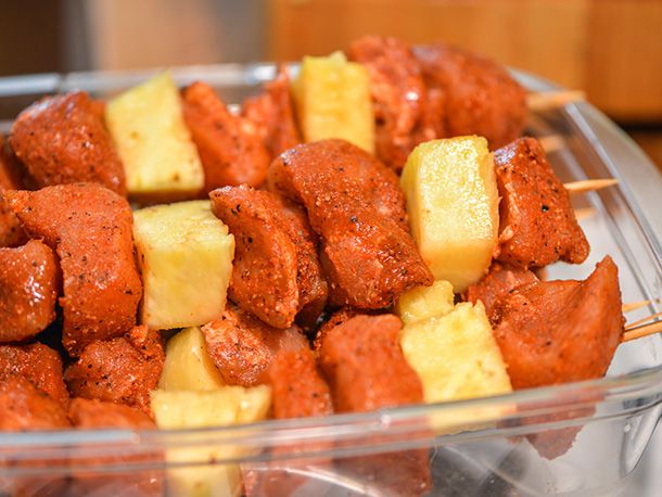 The assembled pork-pineapple skewers piled in a baking dish, ready to be grilled.