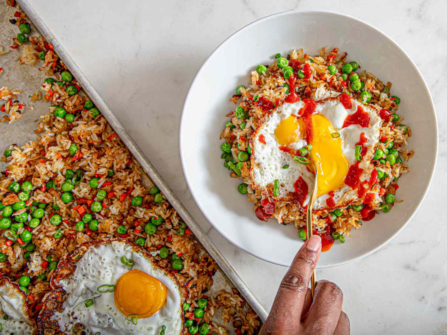 A serving of fried rice with peas and a fried egg on top, being scooped with a spoon from a white bowl