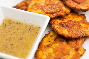 A small dish of mojo sauce next to some tostones. 