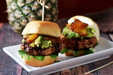 Two mini salmon burgers with pineapple and avocado on a white rectangular plate