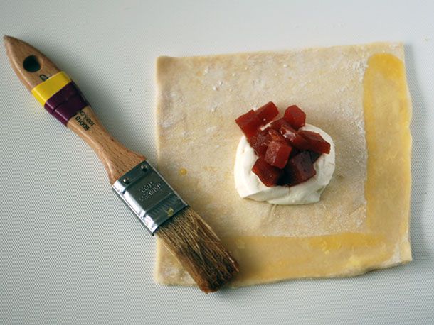 Overhead view of a filling-topped square of puff pastry being brushed with egg wash.