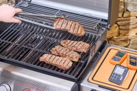 A hand using tongs to lift a steak from the Weber Spirit EP-435 Gas Grill