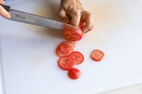 A person thinly slicing tomatoes with a knife