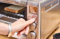 A hand adjusts the settings on a breville compact toaster oven with a slice of bread inside