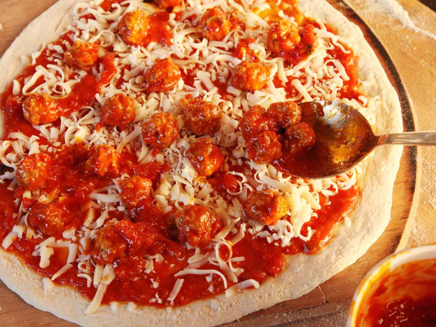 Spooning small meatballs over a tomato sauce– and cheese-topped unbaked pizza