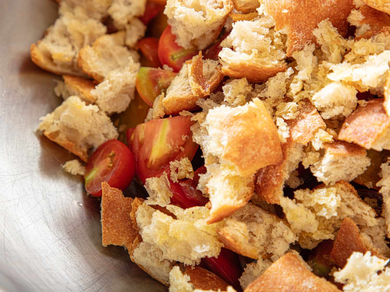 Closeup of torn bread pieces and sliced cherry tomatoes in a bowl