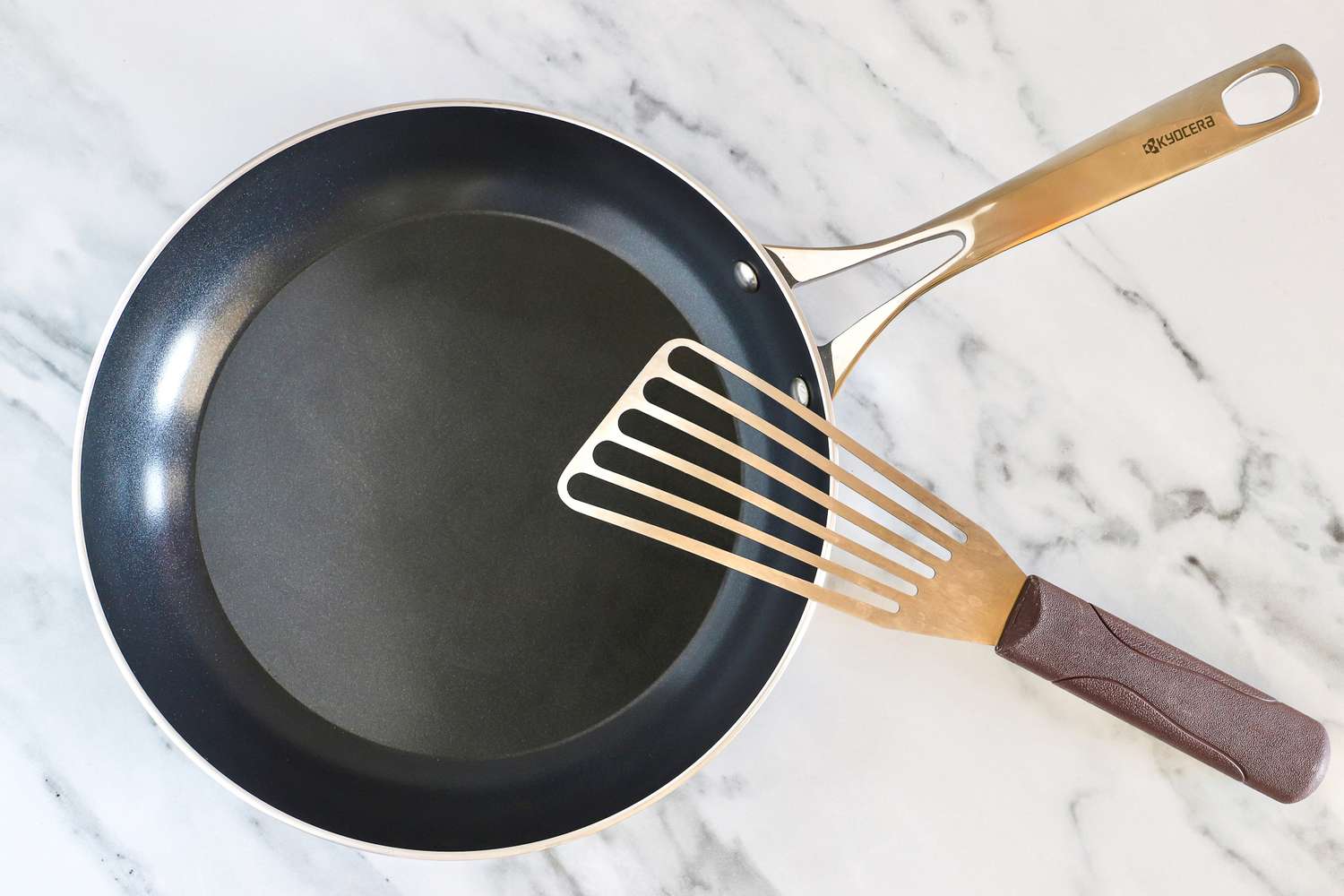 A ceramic frying pan with a metal fish spatula placed on top on a marble surface