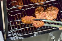 A person smokes meat in the Cuisinart COS-244 Vertical 36-inch Propane Smoker