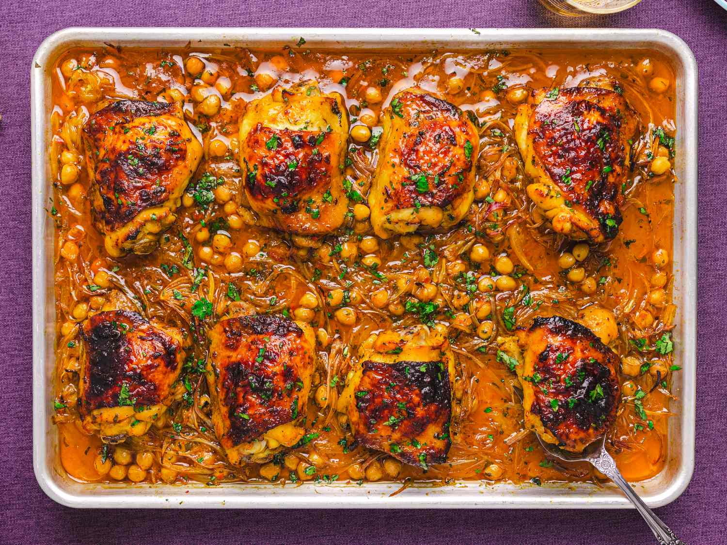 Baked chicken thighs with chickpeas on a tray garnished with herbs in a savory sauce