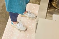 A person stands on The House of Noa Nama Standing Mat while wearing sneakers