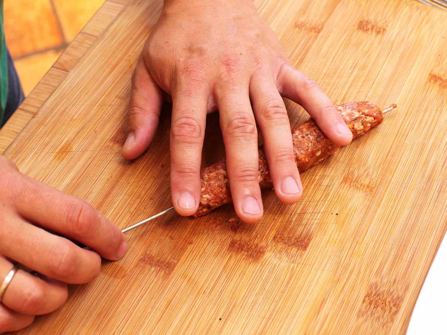 Forming seekh kebab onto skewer on a wooden cutting board. 