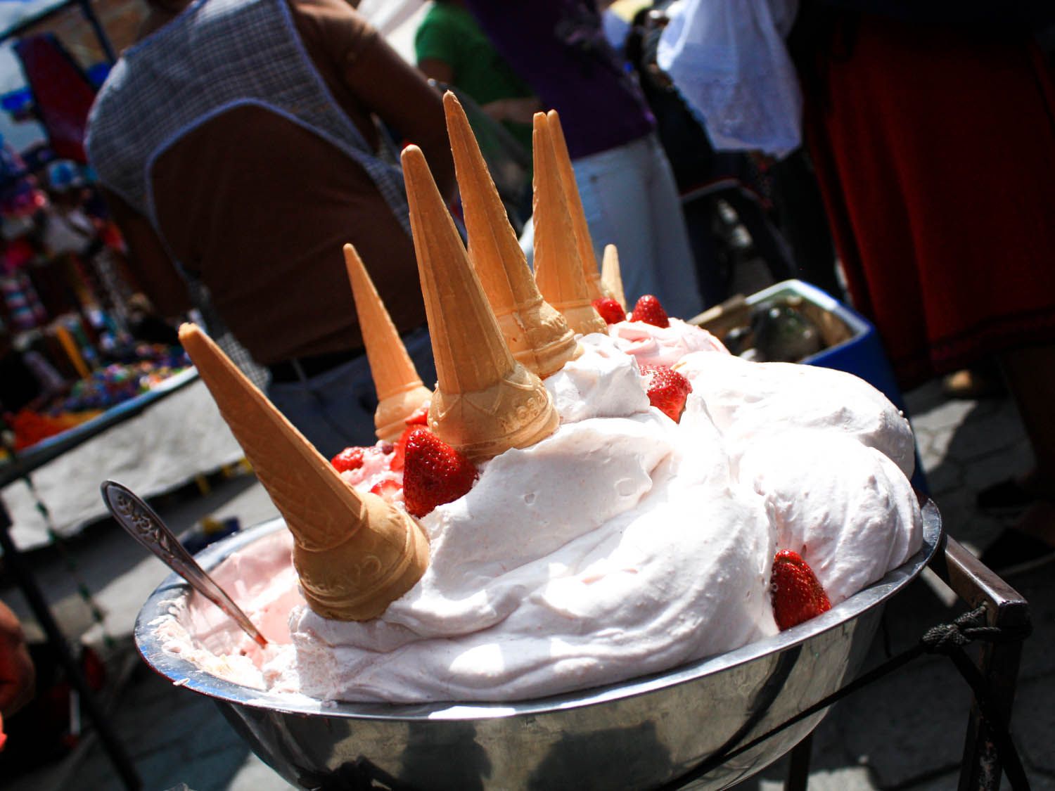 Ecuador's meringue-like espumillas in a bowl with strawberries, cones on top upside down and people in the background.