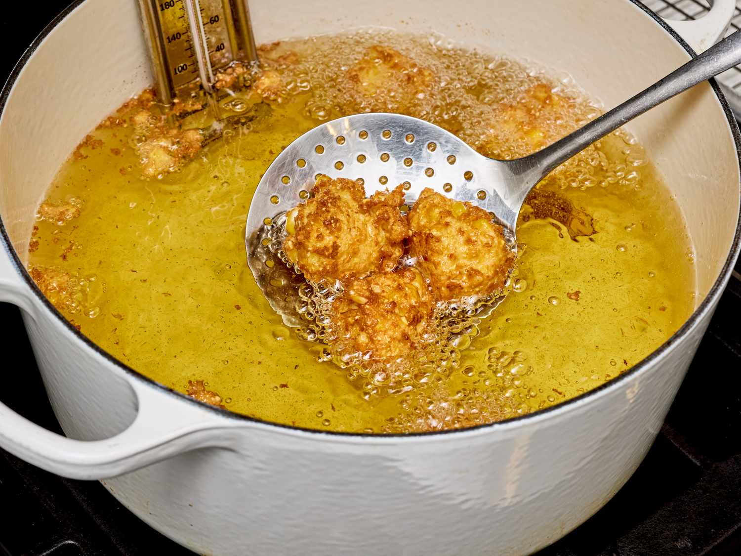 Cooking fritters in hot oil a skimmer lifting some fritters from a pot on the stove