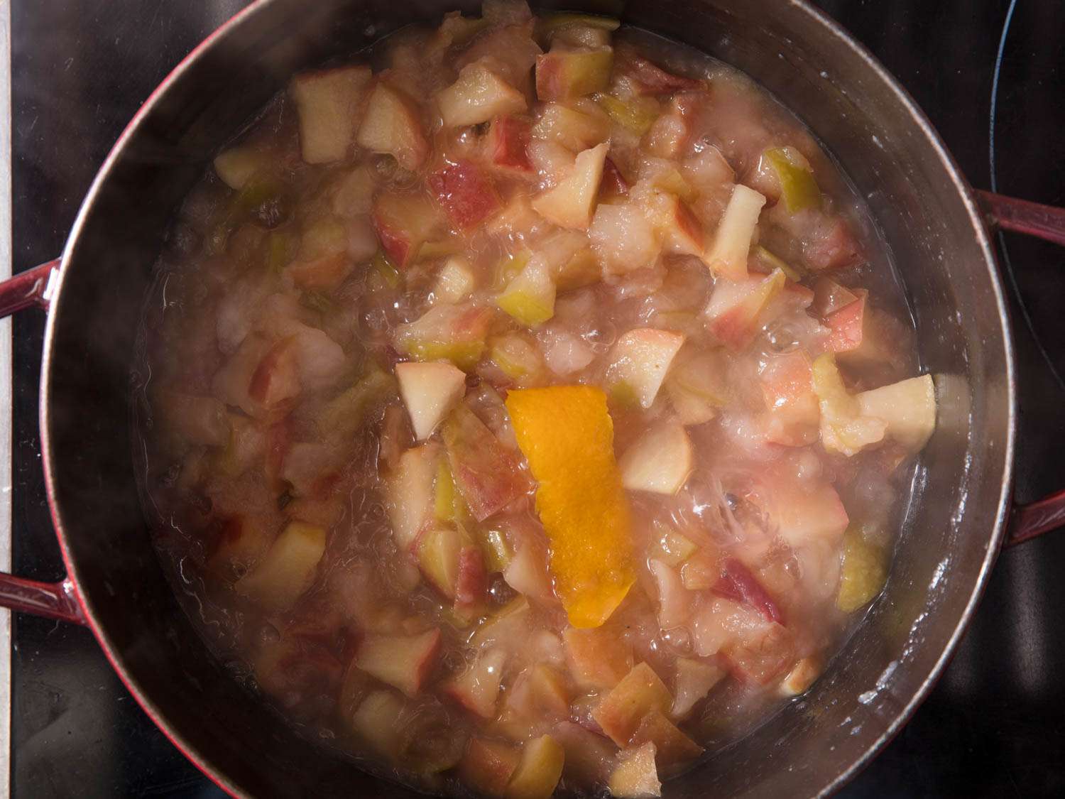 Overhead shot of a pot of cooked apples infused with a strip of orange peel. 