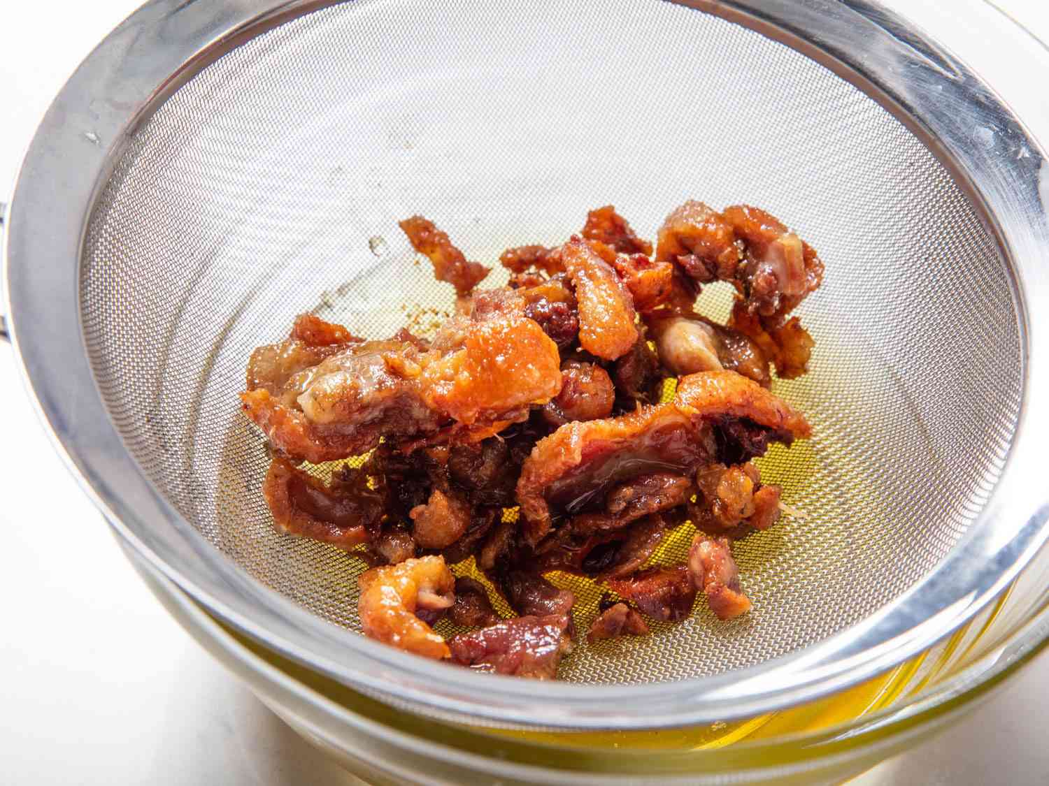 Duck cracklings in a fine-mesh strainer.