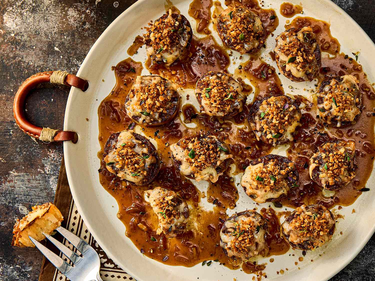Plate of baked appetizers topped with breadcrumbs and a fork with a slice of bread on a table
