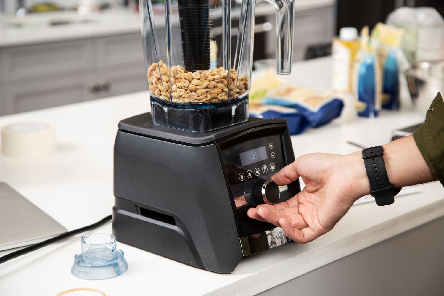 Hand turning a dial on the Vitamix A3500 Ascent Series Professional-Grade Smart Blender filled with peanuts
