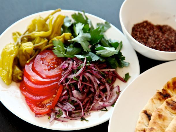 A plate of toppings for the Adana kebab sandwich: sliced tomatoes, sumac onions, pepperoncini, Italian parsley leaves.