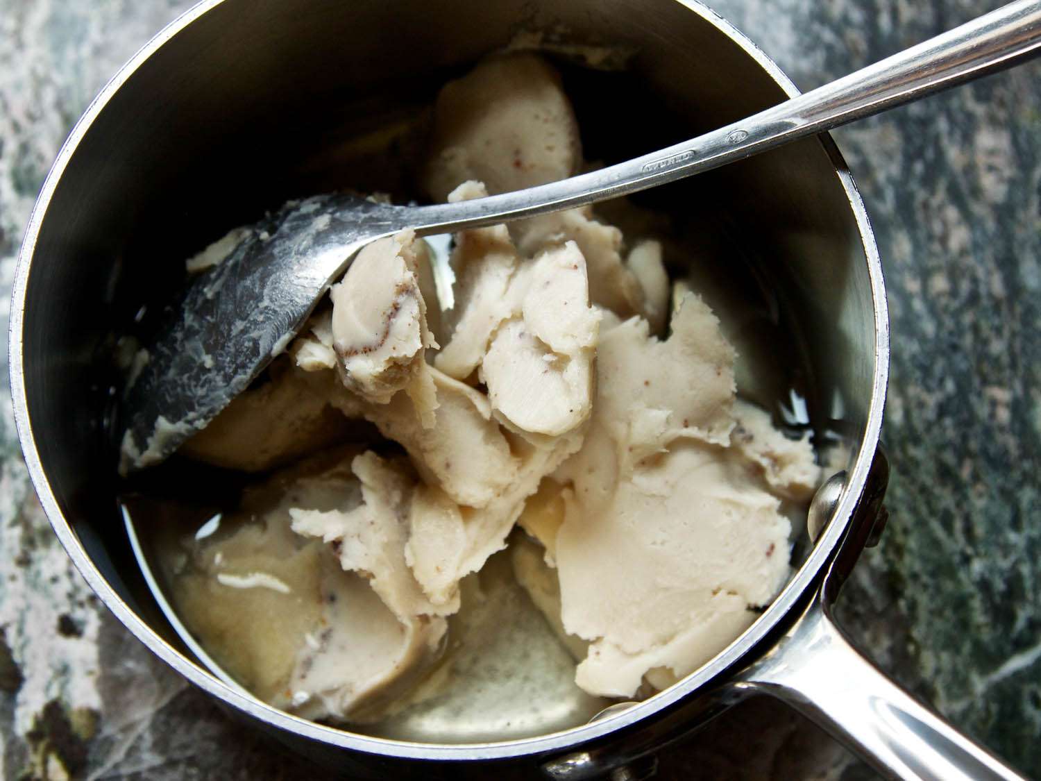 Closeup of solid chunks of bacon fat in a small saucepan.