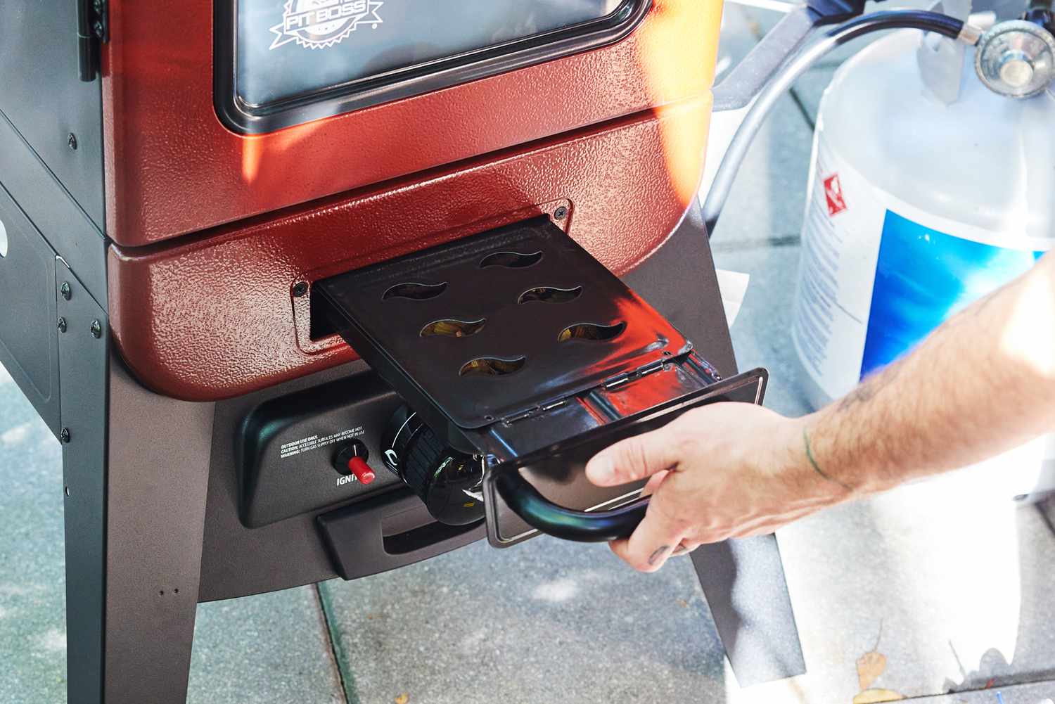 A person filling the wood fuel chamber of the Pit Boss Vertical Propane Grill