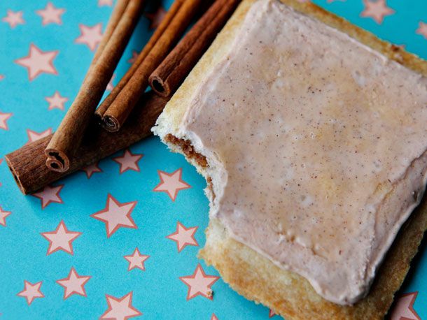 Closeup of a homemade brown sugar cinnamon Pop-Tart, resting next of several sticks of cassia. A bite has been taken out of the corner of the Pop-Tart to reveal the filling inside.