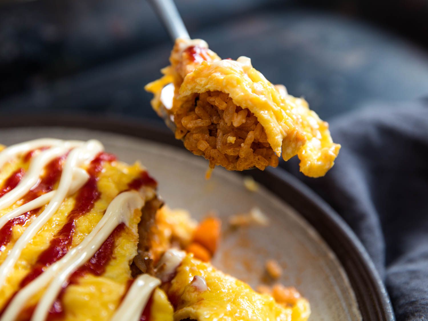 A spoonful lifted from a dish of omurice (fried-rice omelette) with ketchup squeezed on top.