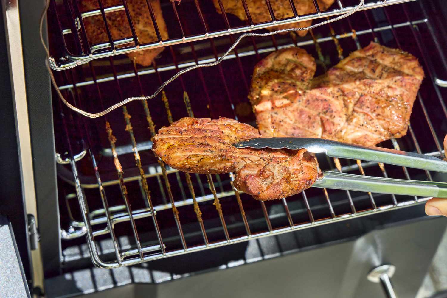 A person smokes meat in the Cuisinart COS-244 Vertical 36-inch Propane Smoker