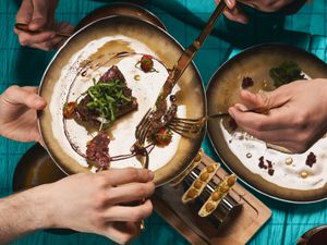 Hands holding utensils and sharing plates of food at a table