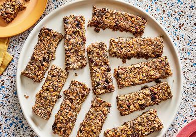 Overhead view of breakfast granola bars on a large plate. The top left has a smaller plate with a broken piece of granola bar on it, and a mug of coffee next to it. 