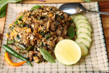 Fried rice with blistered green beans, served on a square patterned plate with cucumber slices and lime.