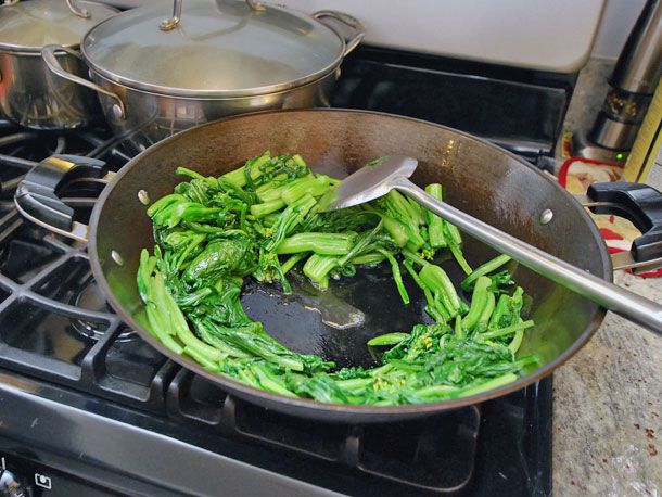 Pressing cooked choy sum to the sides of the wok to clear a space in the middle.
