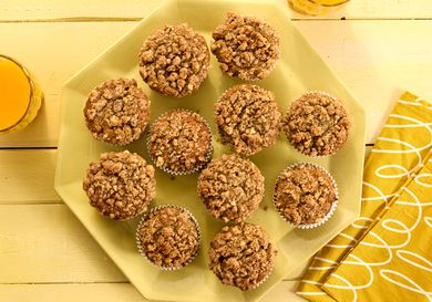 banana nut muffins on a yellow platter, with yellow napkins, a yellow tabletop and orange juice 