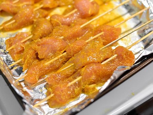 Chicken satay, skewered and resting on a foiled baking sheet.