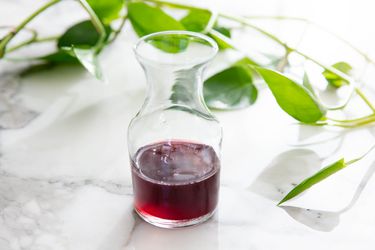 A small glass carafe partially filled with cherry pit syrup. There's a plant vine behind the carafe.