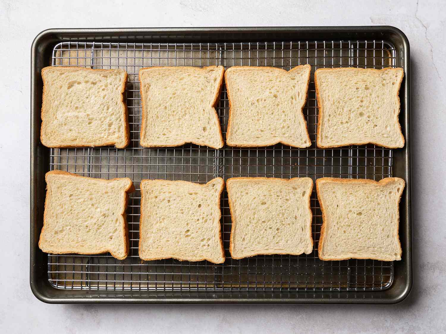 Slices of bread arranged on a wire rack nestled in a baking sheet.