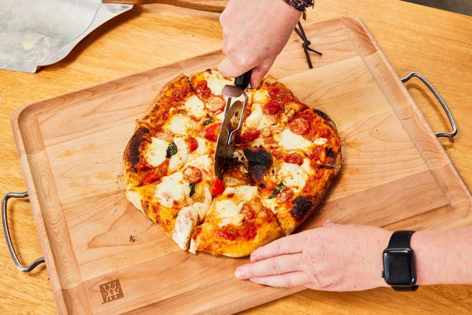 A person slices a pizza on a wooden cutting board.