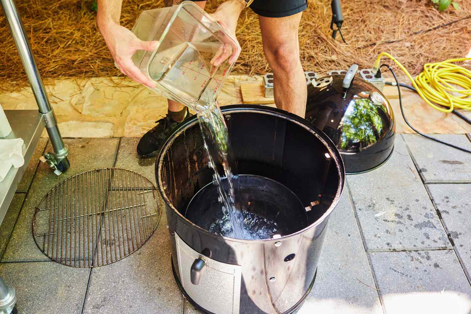 A person pours water into the Weber Smokey Mountain Cooker 18-Inch Charcoal Smoker (721001)