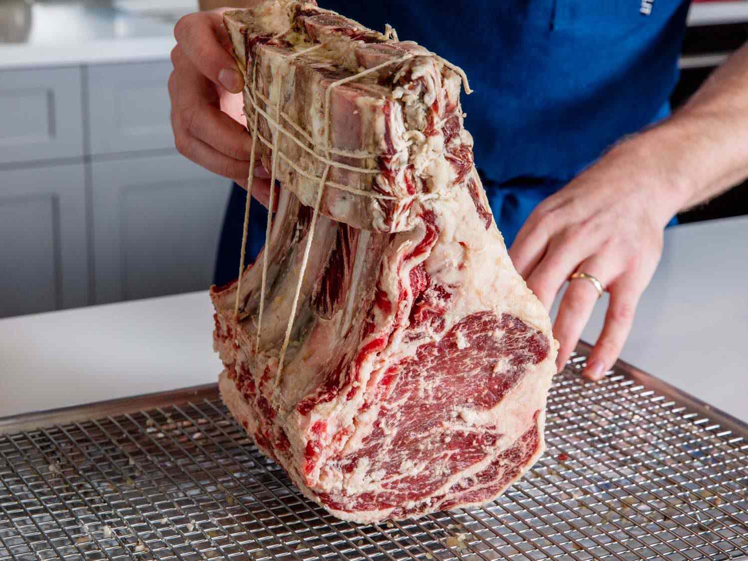 A koji-marinated prime rib held with the rib bones pointed up on a wire rack-lined baking sheet.