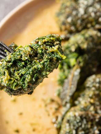 A fork holding a piece of cooked spinach dumpling with more dumplings on a plate in the background