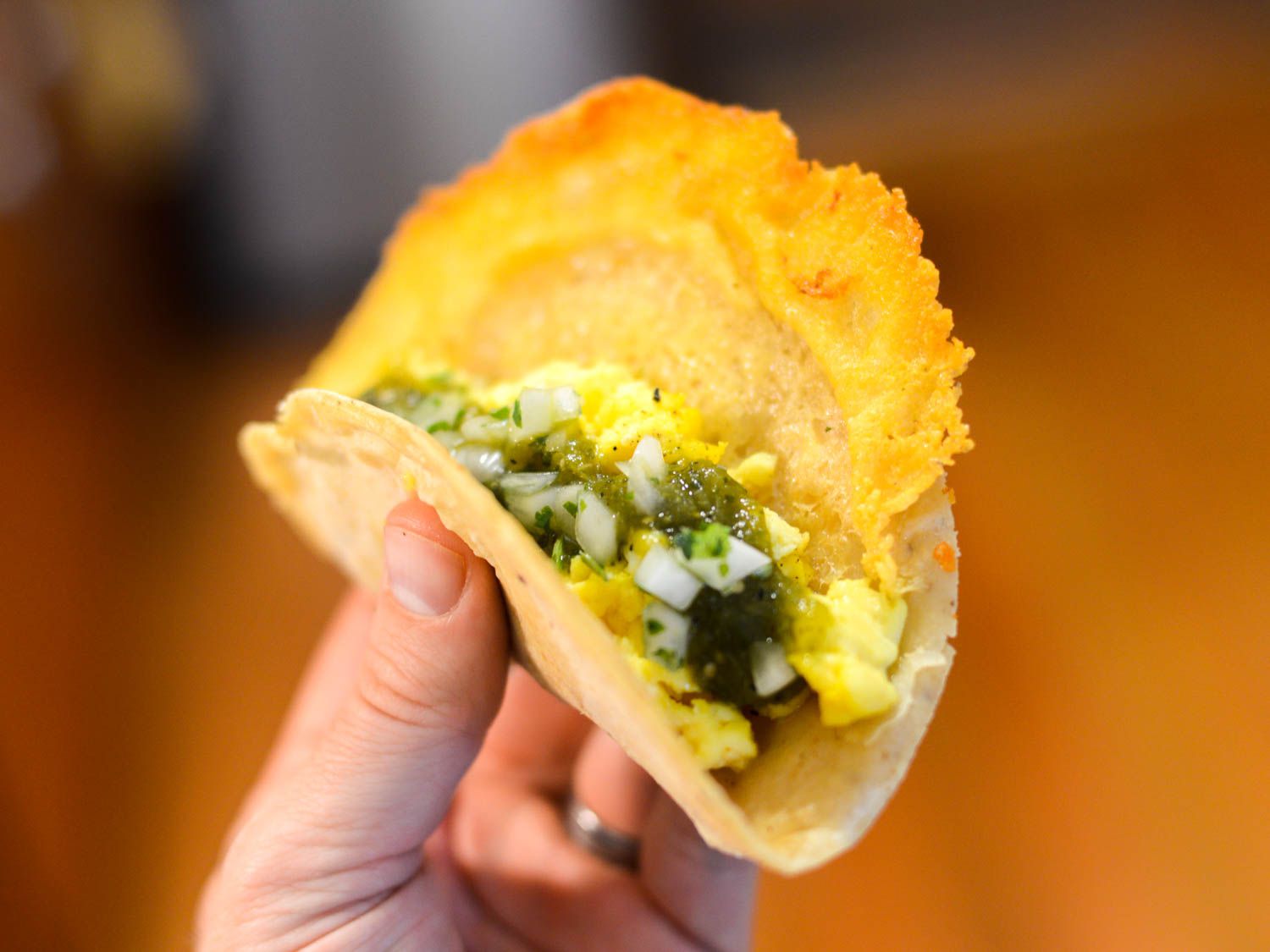 A hand holding a taco overflowing with crispy manchego cheese 